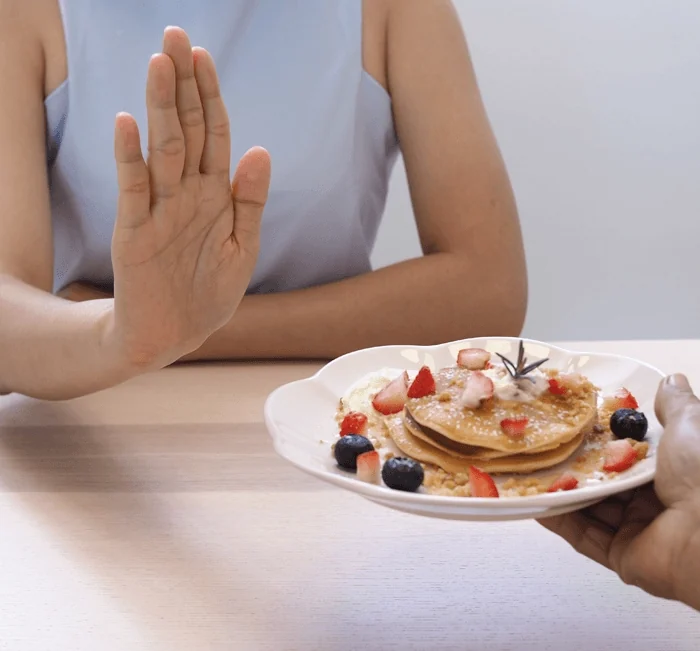 A woman refusing a plate of pancakes, the between-meal appetite moment Gelataro is aimed at