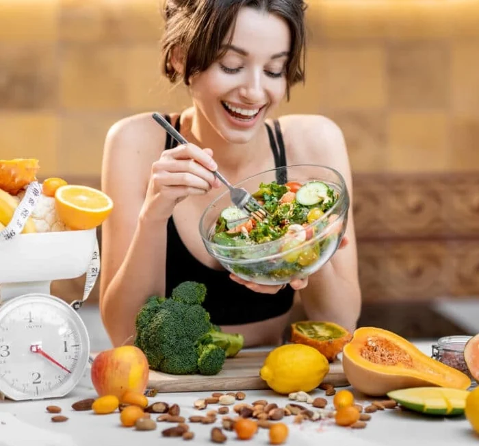 A woman eating a fresh salad surrounded by fruit, vegetables and a kitchen scale, the everyday routine Gelataro is meant to support